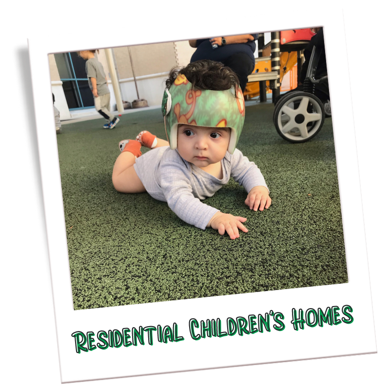 Polaroid of infant boy wearing a helmet with words that say Residential Childrens Homes.
