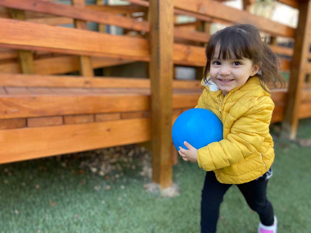 Little girl with special needs runs with blue ball