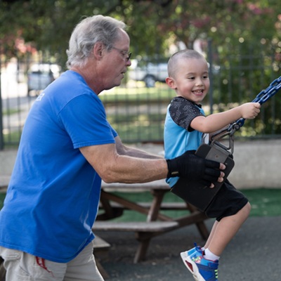 Smiling child on a swing being gently pushed by a caregiver.