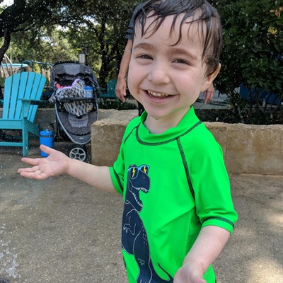 A small child in a green shirt smiles at the camera as he plays in water