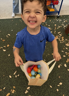 A young boy smiles proudly showing off his bag of collected Easter eggs