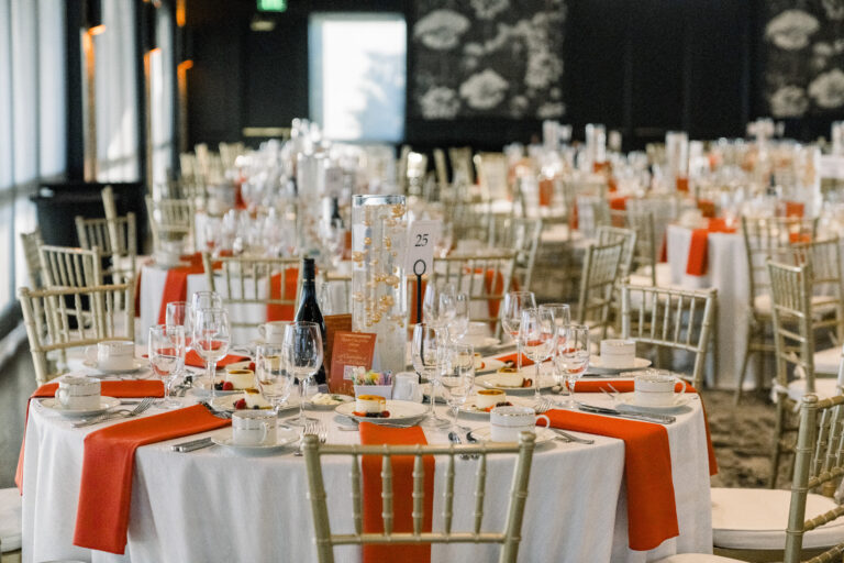 Tables decorated ornately for a gala with white and orange napkins and glassware