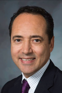 Professional cropped headshot of senator Jose Menendez wearing a suit and smiling at the camera
