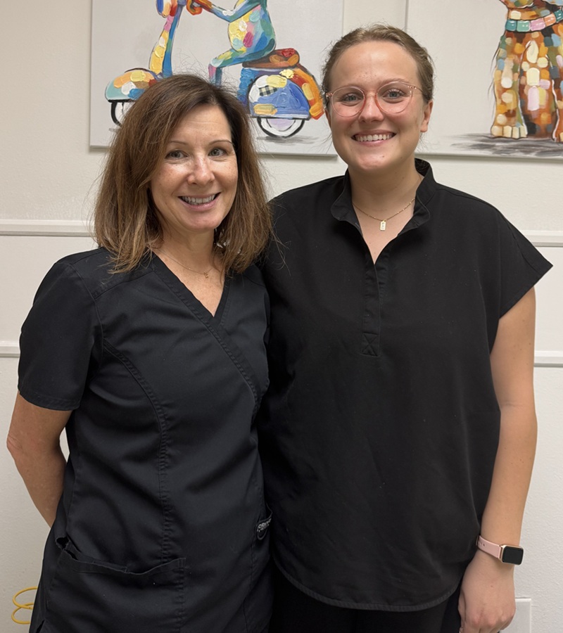 Two female nurses in black scrubs smiling at the camera
