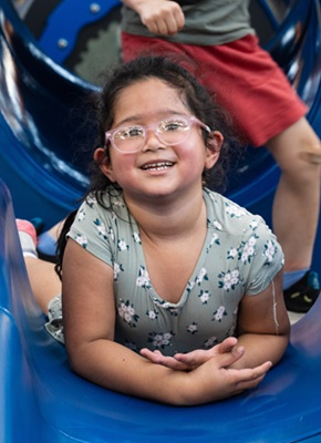 A young girl smiles at the camera from inside a slide