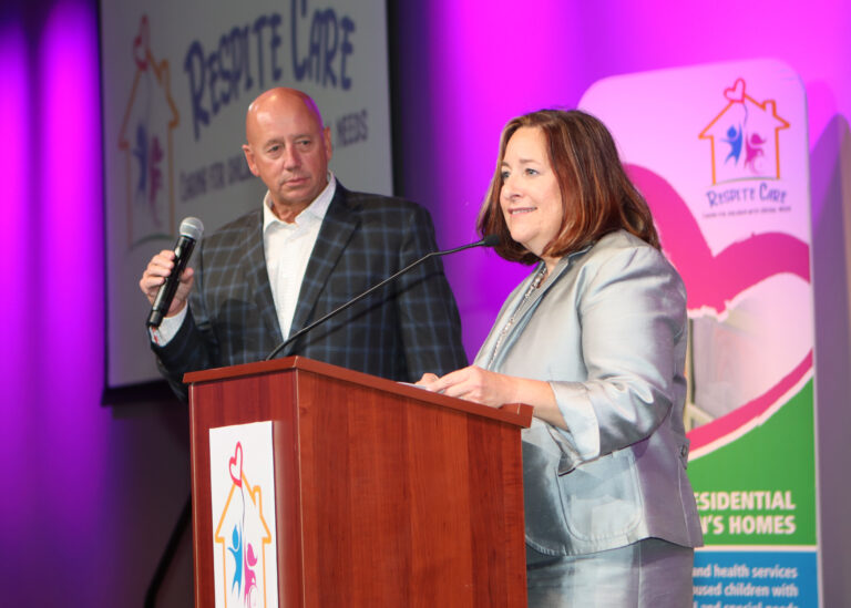 Tom T-Bone Bounds and Rebecca Helterbrand standing at a podium speaking into microphones