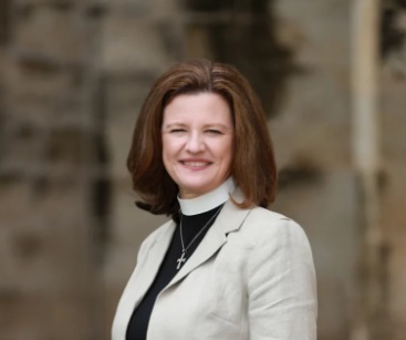 Professional headshot of Rev. Beth Knowlton, wearing a priests collar and white jacket