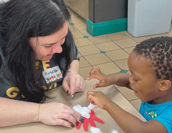 A volunteer and young boy working on a handprint artwork project together