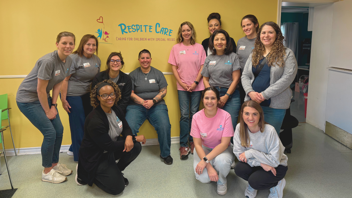 A group of smiling volunteers in front of a yellow wall with Respite Care logo