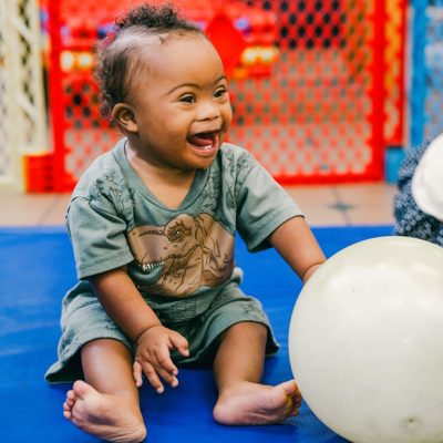 Toddler boy dressed in green laughing while playing with a ball